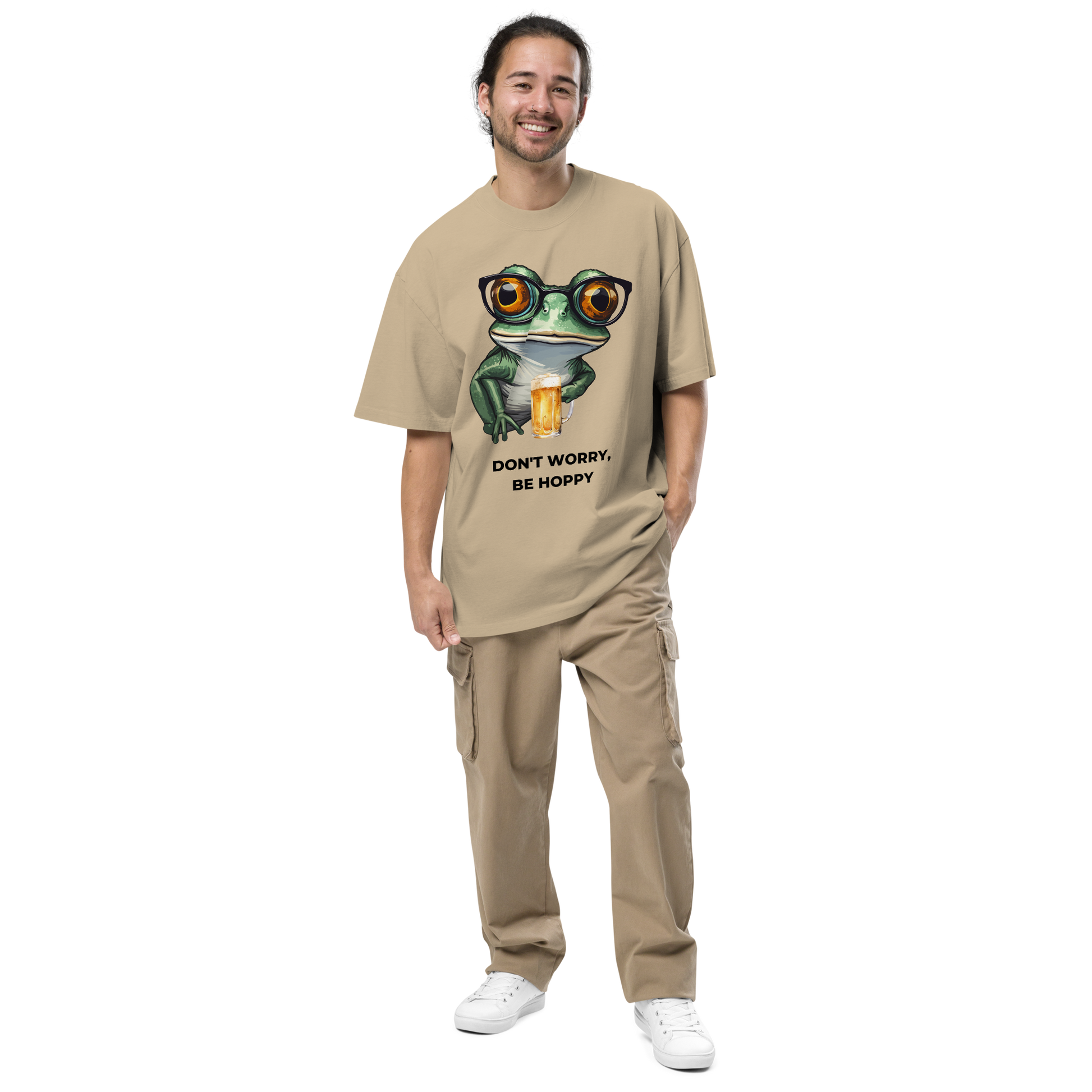 Smiling man wearing a Faded Khaki Frog Oversized T-Shirt featuring a ribbitting Don't Worry, Be Hoppy graphic on the chest - Funny Graphic Frog Oversized Tees - Boozy Fox